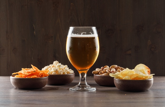 Beer with junk food in a goblet glass on wooden table, side view.