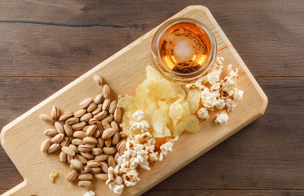 Beer with snack in a goblet glass on wooden and cutting board table, top view.