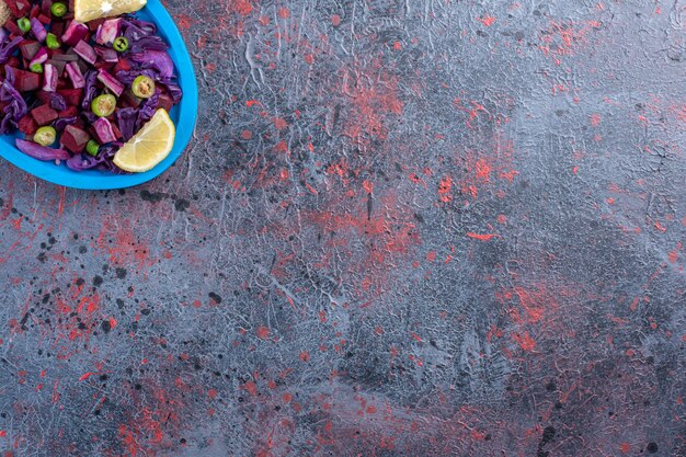 Beet and red cabbage salad on a platter garnished with lemon slices on black table.