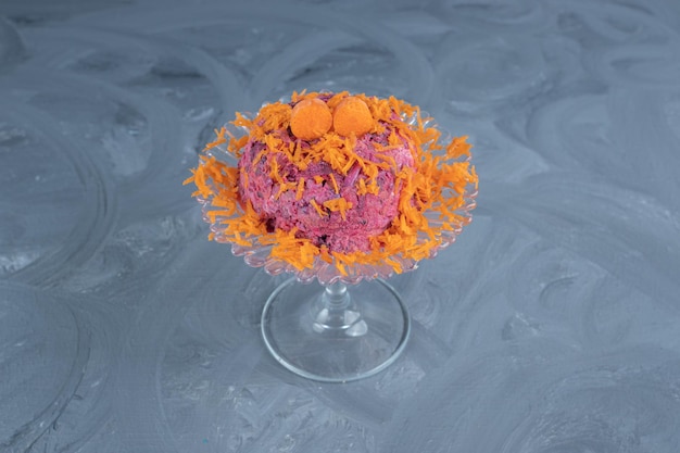 Insalata di barbabietole e noci guarnita con carote e servita su un piedistallo di vetro su una superficie di marmo.