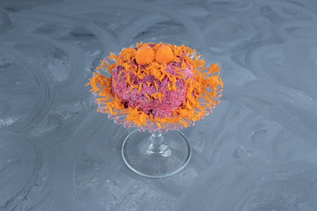 Beet and walnut salad garnished with carrot and served on a glass pedestal on marble surface.