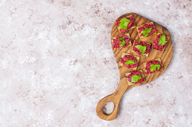 Beetroot hummus canapes withgreen pepper slices and parsley on cutting board on light surface