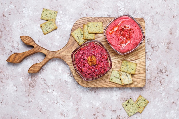 Beetroot hummus on cutting board with salty cookies on light surface