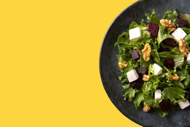 Салат из свеклы с сыром фета, листьями салата и грецкими орехами на желтом фоне