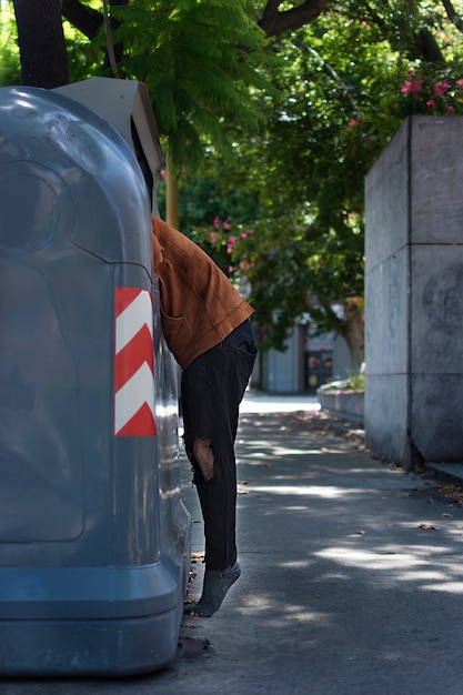 Beggar looking through trash bins in the streets