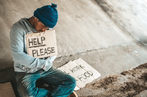 Foto gratuita mendicanti seduti sotto il ponte con un cartello, aiutano per favore.