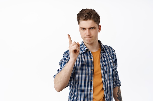 Behave yourself. Strict young man scolding bad behaviour, shaking finger in warning, prohibit or dislike something, disappointed, standing against white background. Copy space