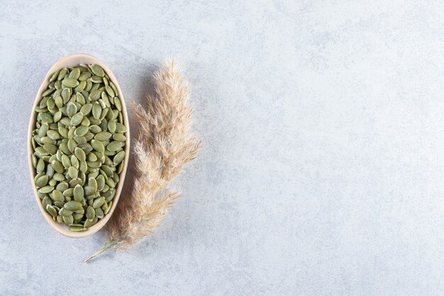 Beige bowl of peeled pumpkin seeds on stone background.