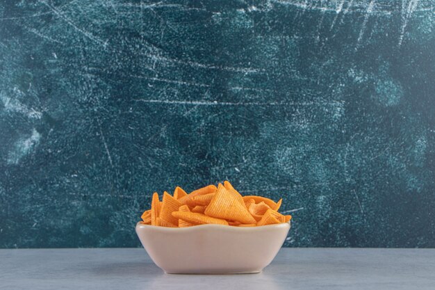 Beige bowl of triangle shaped crispy chips on stone background.