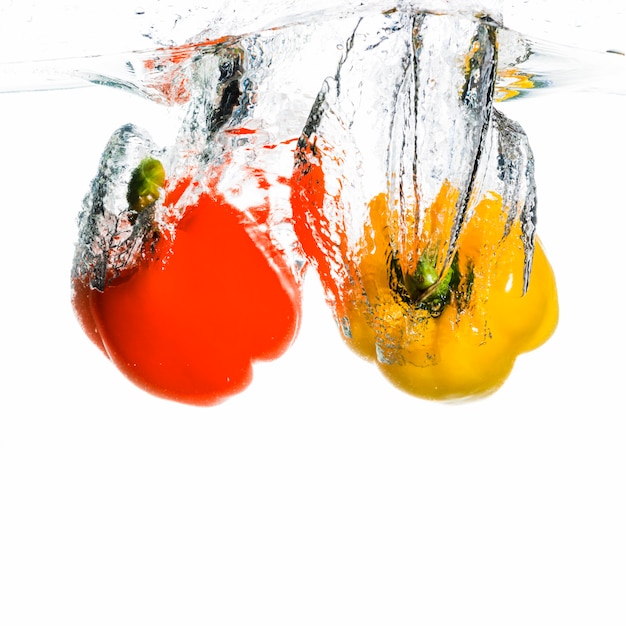 Bell pepper falling into water forming splash against white background