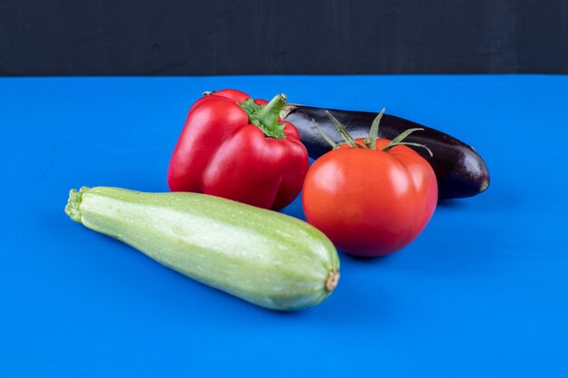 Bell pepper, tomato, eggplant and zucchini on blue surface