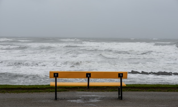 Free photo bench on the beach surrounded by the sea under a cloudy sky during the storm