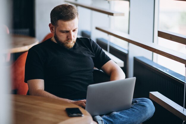 Бородатый мужчина работает на ноутбуке в кафе