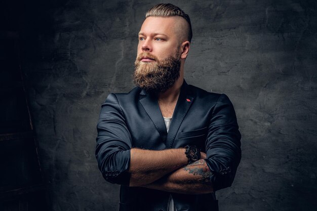 Berded hipster male with crossed arms dressed in violet suit on grey vignette background.