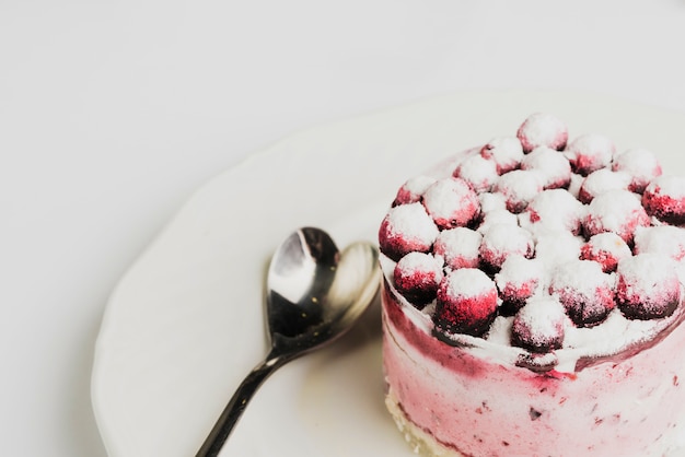 Free photo berries toppings on round cake with stainless spoon on plate against white backdrop