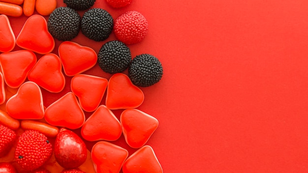 Free photo berry fruit and heart shape candies on red background