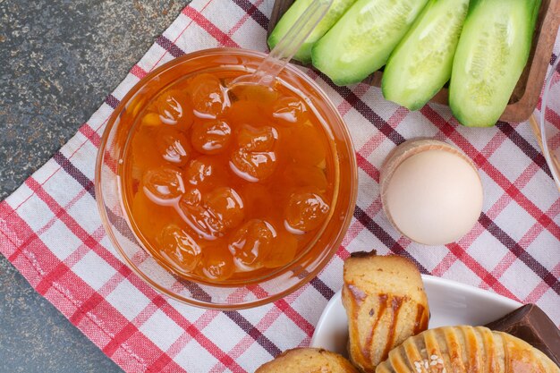 Foto gratuita marmellata di frutti di bosco, biscotti, uova e fette di cetriolo sulla tovaglia.