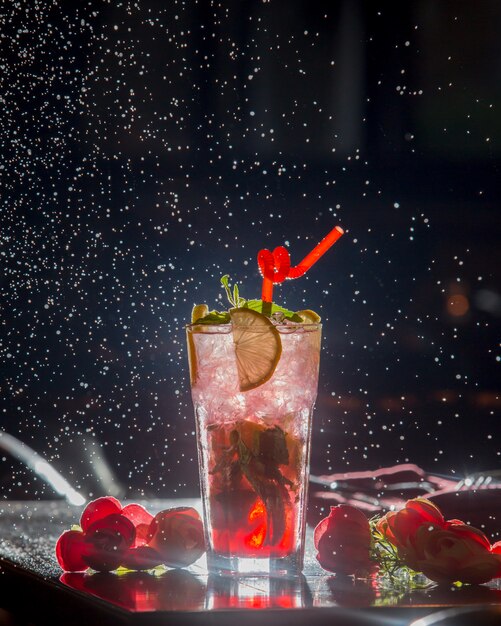 Berry lemon cocktail with red pipe and ice cubes in black starry background.