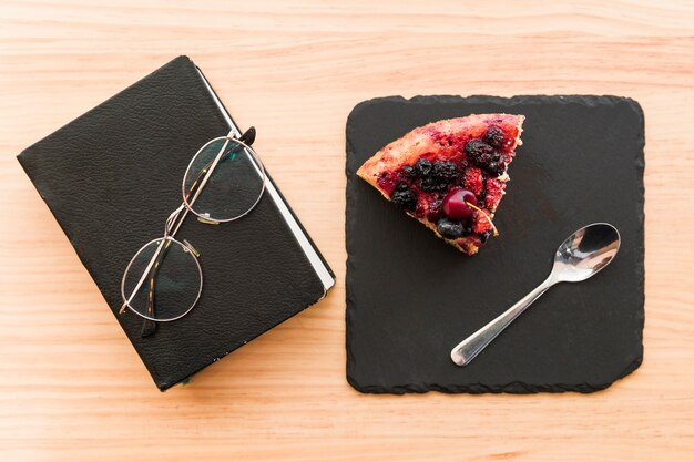 Berry pastry near diary and spectacles on wooden desk