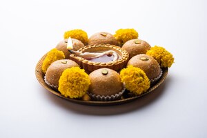 besan ladoo and diwali diya or clay lamp decorated in a plate with marigold flowers - happy diwali greeting