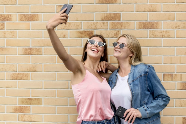 Free photo best friends taking a selfie with their sunglasses on