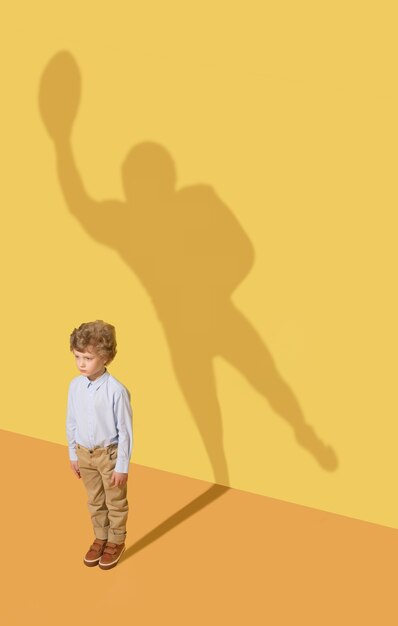 チームの最高のメンバー。子供の頃と夢のコンセプト。黄色のスタジオの壁に子供と影の概念的なイメージ。小さな男の子はアメリカンフットボール選手になり、スポーツのキャリアを築きたいと思っています。