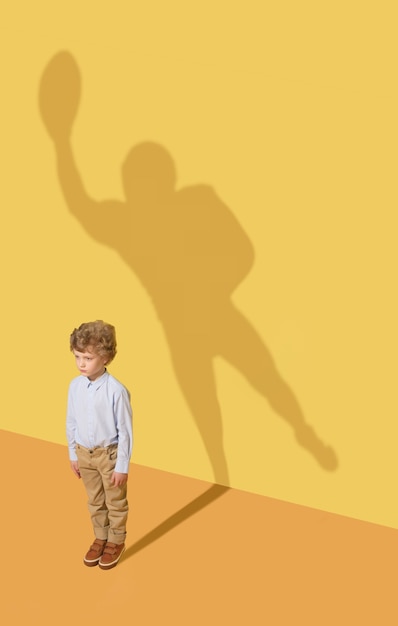 Best member of the team. Childhood and dream concept. Conceptual image with child and shadow on the yellow studio wall. Little boy want to become american football player and to build a sport career.