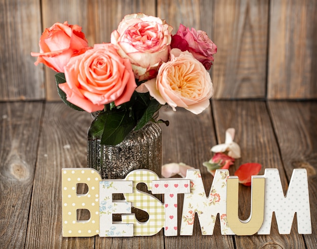 Best Mum written in multicolored wooden letters and fresh rose in glass vase. Spring and mother's day concept.