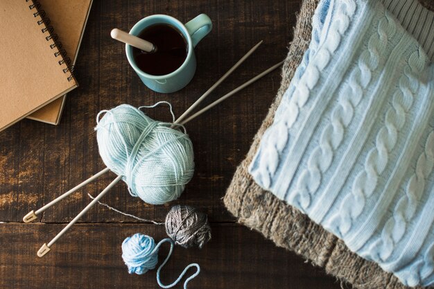 Beverage and notebooks near knitting supplies and warm clothes