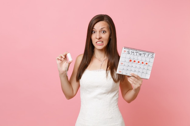La donna preoccupata e sconcertata in abito bianco tiene il calendario dei periodi femminili con tampone per controllare i giorni delle mestruazioni
