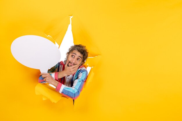 Bewildered young guy holding white balloon and posing for camera in a torn hole and free background in yellow paper