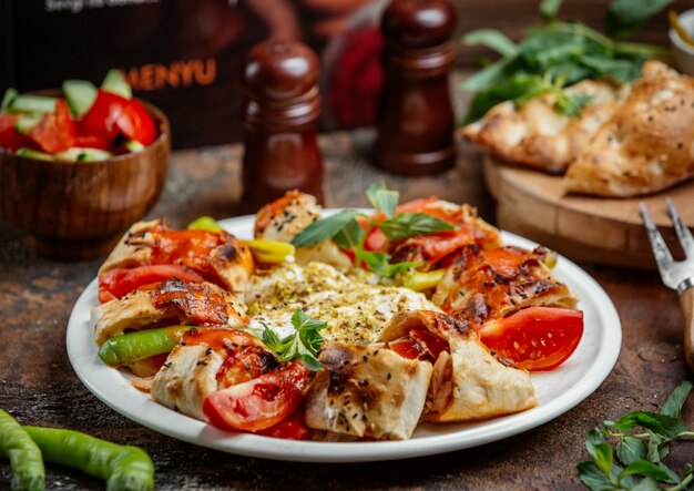 Beyti wrapped kebab topped with tomato sauce, served with tomato, pepper, yoghurt