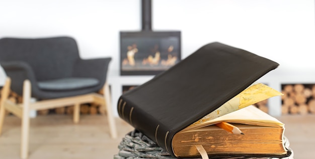 Книга Библии с карандашом, на фоне гостиной с камином. Чтение книги в уютной обстановке. Закройте вверх.
