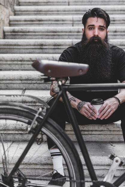 Bicycle in front of a man sitting on staircase holding coffee cup