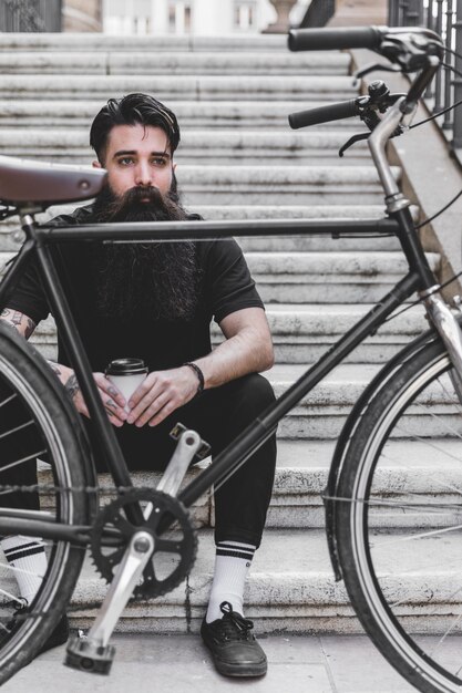 Bicycle in front of a young man sitting on staircase holding takeaway coffee cup