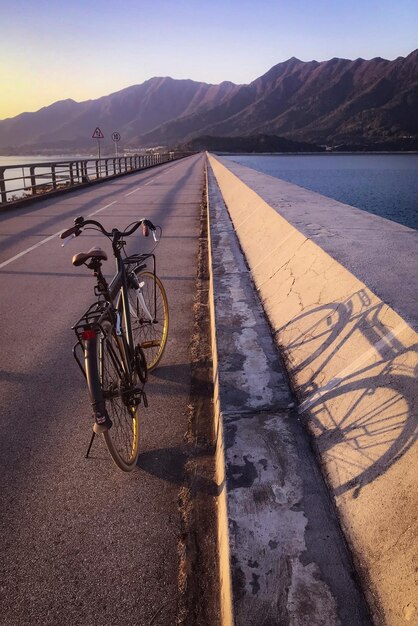 Bicycle standing on the asphalt road on the background of the ocean and mountains at sunset