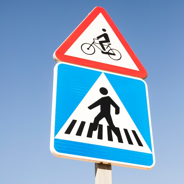 青空に対して道路標識を横断する現代の正方形の歩行者の上の自転車の警告サイン