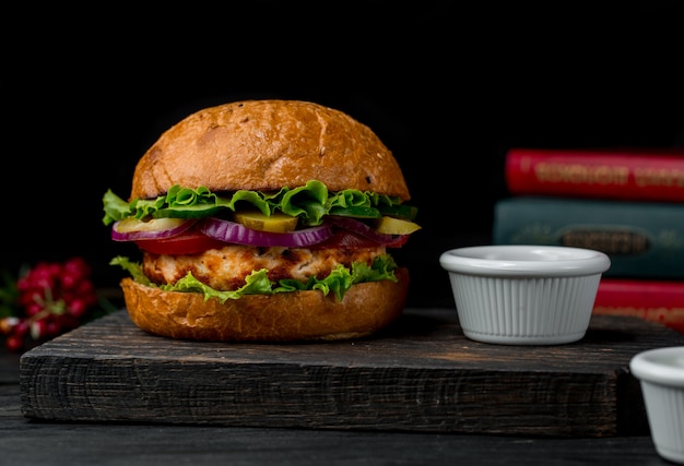 Big burger stuffed with chicken meat and salad on a wooden board.