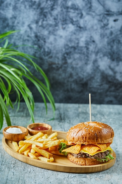 Foto gratuita grande hamburger con patate fritte nel piatto di legno sulla superficie di marmo