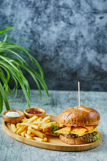 Big burger with fry potato in the wooden plate on the marble surface 