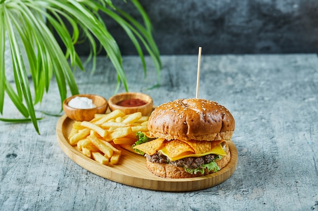 Grande hamburger con patate fritte nel piatto di legno sulla superficie di marmo