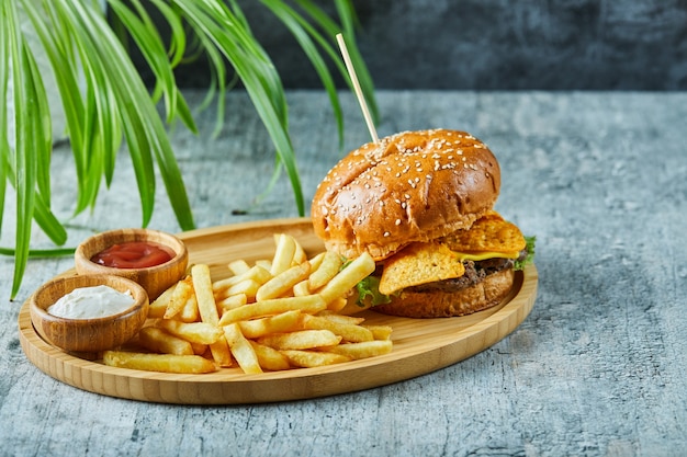 Big burger with fry potato in the wooden plate on the marble surface 