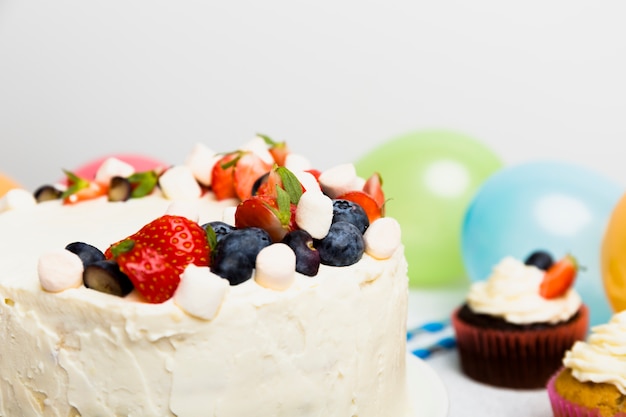 Big cake with different berries near cupcakes on table