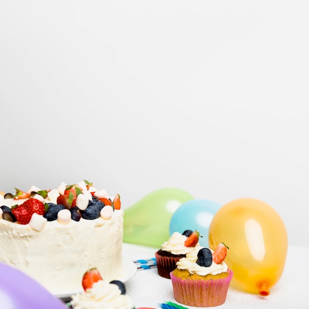 Big cake with different berries near cupcakes 