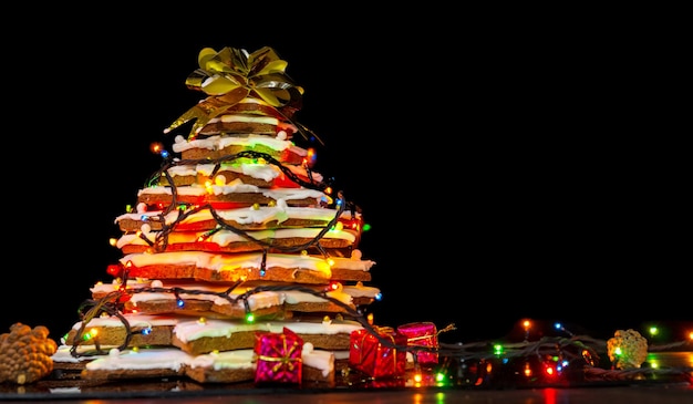 暗い​背景​に​ライト​が​付いている​大きな​自家製​ジンジャーブレッド​の​クリスマスツリー​。​季節​限定​の​オファー​と​ホリデーポストカード​の​モックアップ