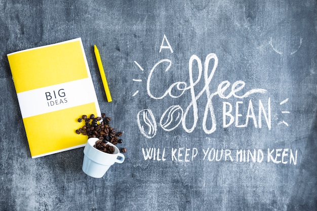 Free photo big ideas book with spilled coffee beans from cup and text on blackboard