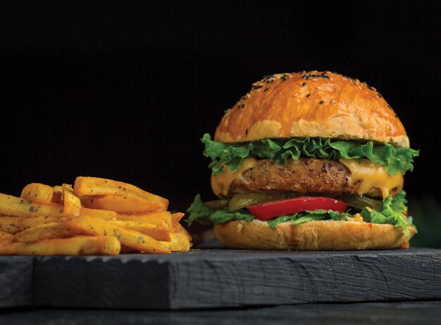 Big mac burger and potatoes sticks on a dark wooden board.