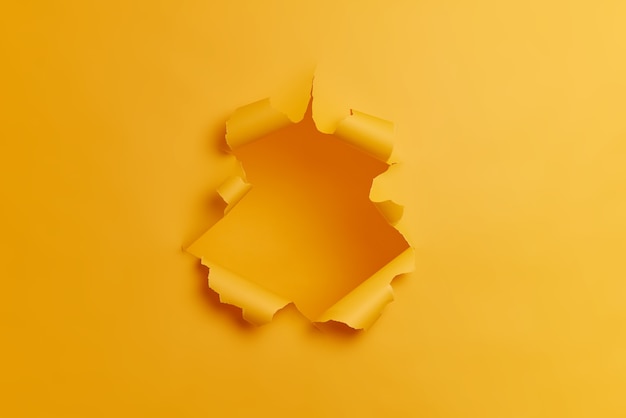 노란색 배경의 중앙에 큰 종이 구멍. 찢어진 찢어진 된 스튜디오 벽. 획기적인 개념. 총에 사람이 없습니다.
