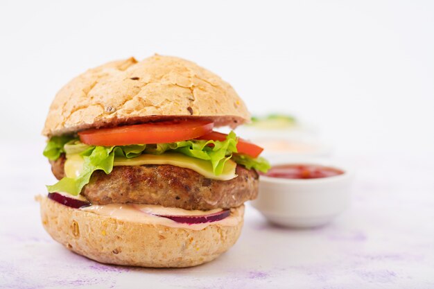 Big sandwich - hamburger with juicy beef burger, cheese, tomato, and red onion on light table and French fries.