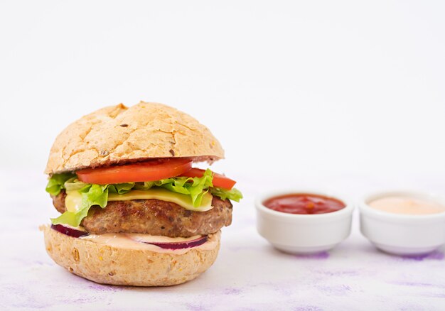 Big sandwich - hamburger with juicy beef burger, cheese, tomato, and red onion on light table and French fries.